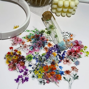 Flat lay of colorful floral PET stickers with earbuds and candles on white background