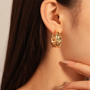 Macro side view of gold C-shaped twisted earrings with irregular hammer texture on model