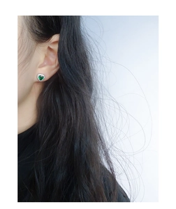 Close-up of heart-shaped emerald green earrings with zircon halo on model's ear