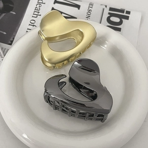 Irregular heart-shaped metal hair clips in gold and gunmetal grey on ceramic plate