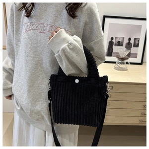 Detail of black corduroy tote bag featuring adjustable strap and white button closure