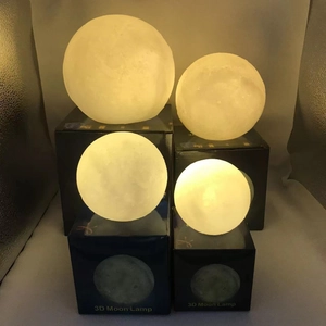 Four different sized 3D Moon Lamps with warm yellow glow on black retail packaging boxes