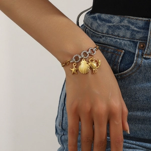 Detail of gold chain bracelet featuring starfish, seashell and crab charms on a model