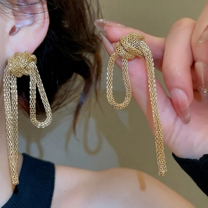 Detail of gold woven mesh knot earrings with long tassels and intricate metallic texture