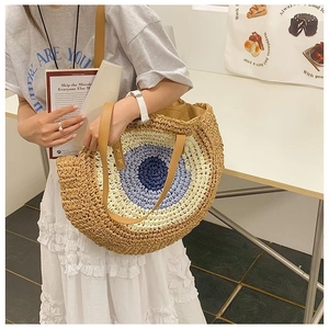 Detail of bohemian woven straw bag with blue evil eye pattern and brown leather handles