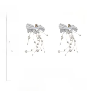 Détail de boucles d'oreilles nœud en dentelle avec strass et longs glands perles