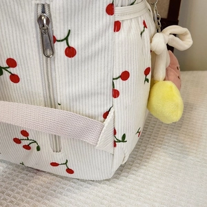 Detail of white corduroy backpack with red cherry print and smooth metal zipper
