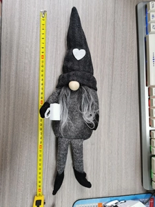 Detail view of a grey knitted gnome Christmas ornament being measured with a yellow tape rule