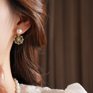 Close-up of gold-plated earrings with mother-of-pearl, blue gems, and compass star charms
