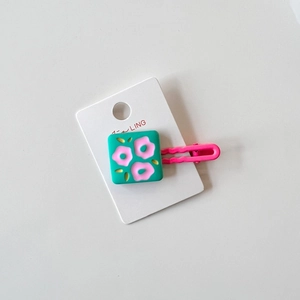 Detail of pink metal hair clip with a green floral resin square on a white display card