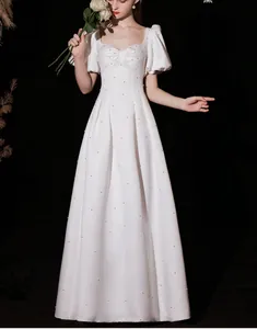 Detail of square neck white gown with hand-applied pearls and puff sleeves on black background