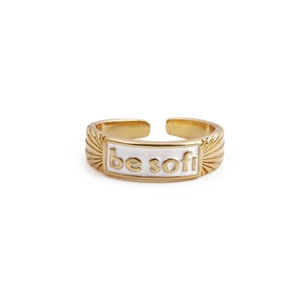 Detail of gold-plated open ring featuring white enamel patch with be soft lettering
