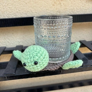 Macro shot of a handmade crochet turtle coaster holding a textured glass on a shelf