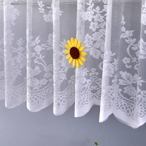 Close-up of white lace curtain featuring floral embroidery and sunflower decorative pendant