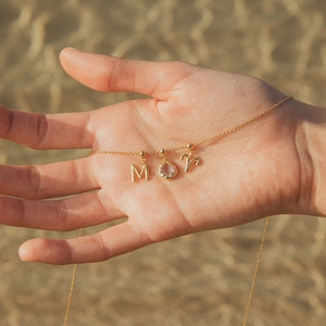 Collier doré avec pendentifs lettres M et R et pierre en cristal tenu par une main