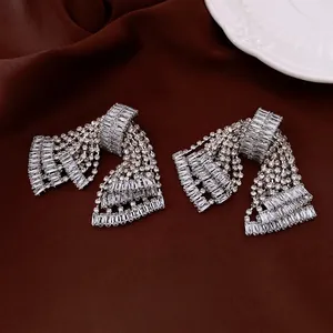 Silver bow tassel earrings with sparkling baguette diamonds on brown silk fabric