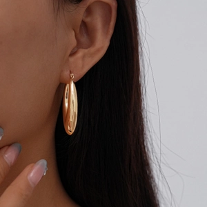 Macro view of large golden teardrop hoop earrings with polished metallic finish on model