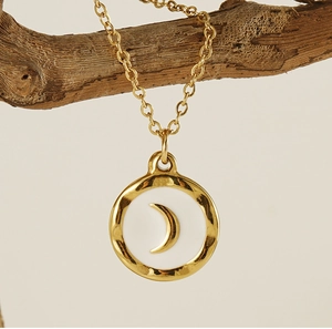 Detail of gold moon pendant necklace hanging on a branch with hammered texture edges