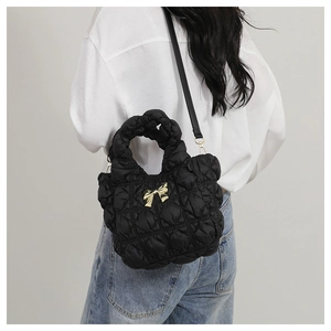 Detail of a black quilted cloud bag showing the gold bow ornament and twisted handle