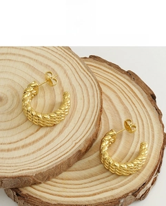Detailed close-up of 18k gold-plated C-shape twisted hoop earrings on wood surface