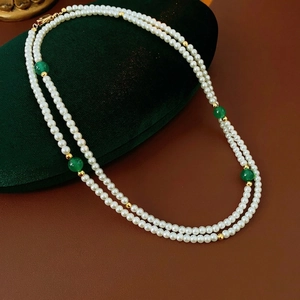 Double-layered pearl necklace with green agate beads on a dark velvet display pad