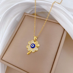 Elegant gold clover devil eye necklace with crystals displayed on beige jewelry box