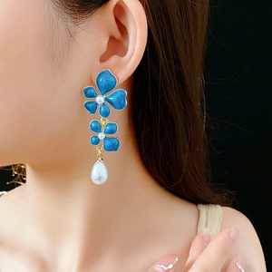 Detail of blue enamel flower earrings with white pearl drop on model with black background