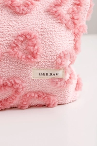 Gros plan d'une trousse à maquillage en sherpa rose avec cœurs rouges et étiquette