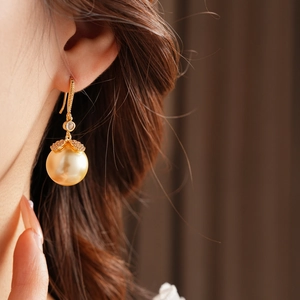 Gros plan sur boucle d'oreille dorée en perle avec détails fleur en zircone sur modèle