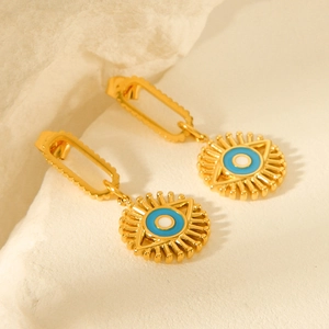 Golden Evil Eye drop earrings with blue and white enamel on a textured stone background