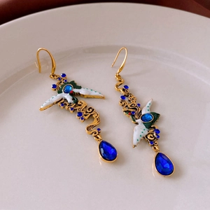 Detail of crane earrings with white enamel wings and teardrop blue gemstones