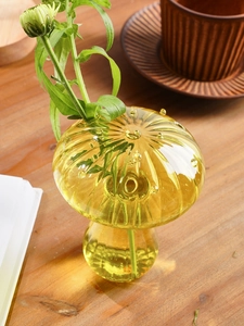 Close-up of yellow mushroom glass vase with natural bubbles and green plant stems