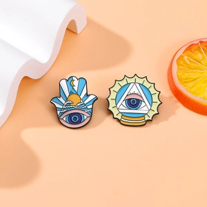Creative Hamsa and All-seeing Eye enamel pins on an artistic orange themed background