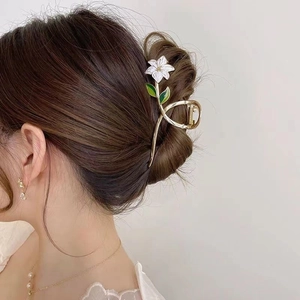 Detail of white lily flower hair claw clip with green leaves on golden alloy base
