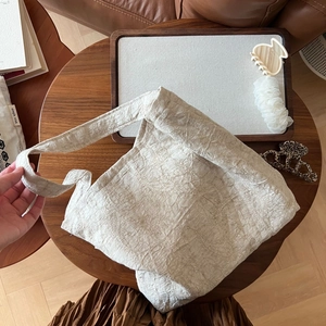Détail d'un sac bandoulière plissé crème sur une table en bois avec des accessoires