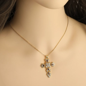 Close-up of a gold cross necklace with a red heart-shaped gemstone worn by a model