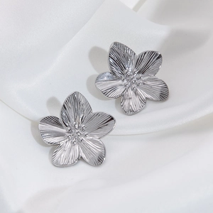 Detailed macro view of silver flower stud earrings with textured petals on white silk
