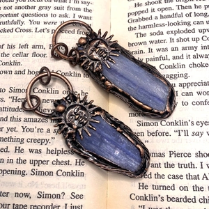 Detail van een vintage bronzen hanger met blauwe kyanietsteen en zonnemotief op boek