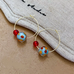 Detail of gold hoop earrings with red translucent beads and spotted resin ball pendants