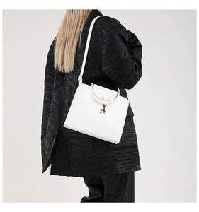 Close-up of white crocodile pattern handbag with gold handle on a black textured coat