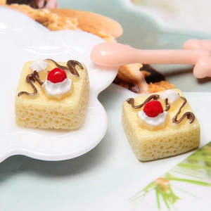 Macro shot of miniature resin square cake with cream, cherry and chocolate decoration