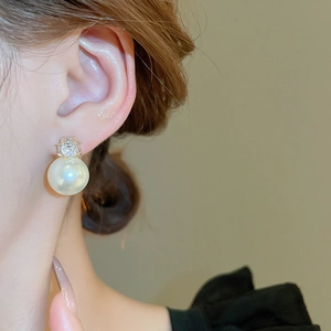 Close-up of a minimalist silver stud earring with a glossy pearl and zircon on a model