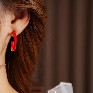 Close-up of elegant red C-shaped hoop earrings on a model with glossy enamel finish
