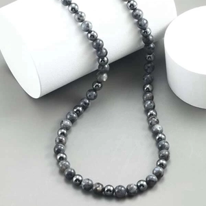 Close-up of beaded necklace with gray tiger eye stones on white geometric pedestals