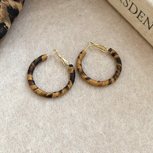 Detail of round leopard print earrings with gold metal accents on beige felt texture