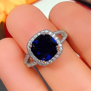 Macro shot of silver ring featuring square blue center stone and halo of white crystals