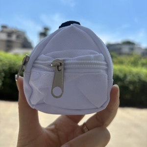 Close-up of a white canvas mini backpack keychain with silver zippers and black lanyard clip