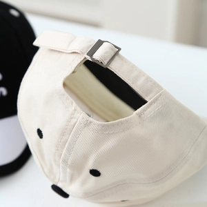 Detail view of the beige cotton baseball cap featuring an adjustable metal buckle back