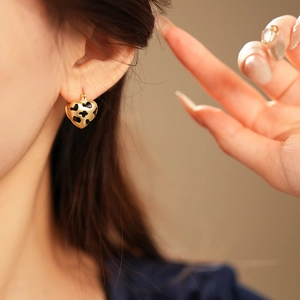 Close-up of golden heart-shaped earrings with black leopard print pattern on model