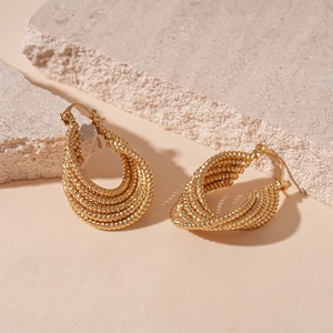 Close-up of golden multi-layered geometric oval hoop earrings on textured stone